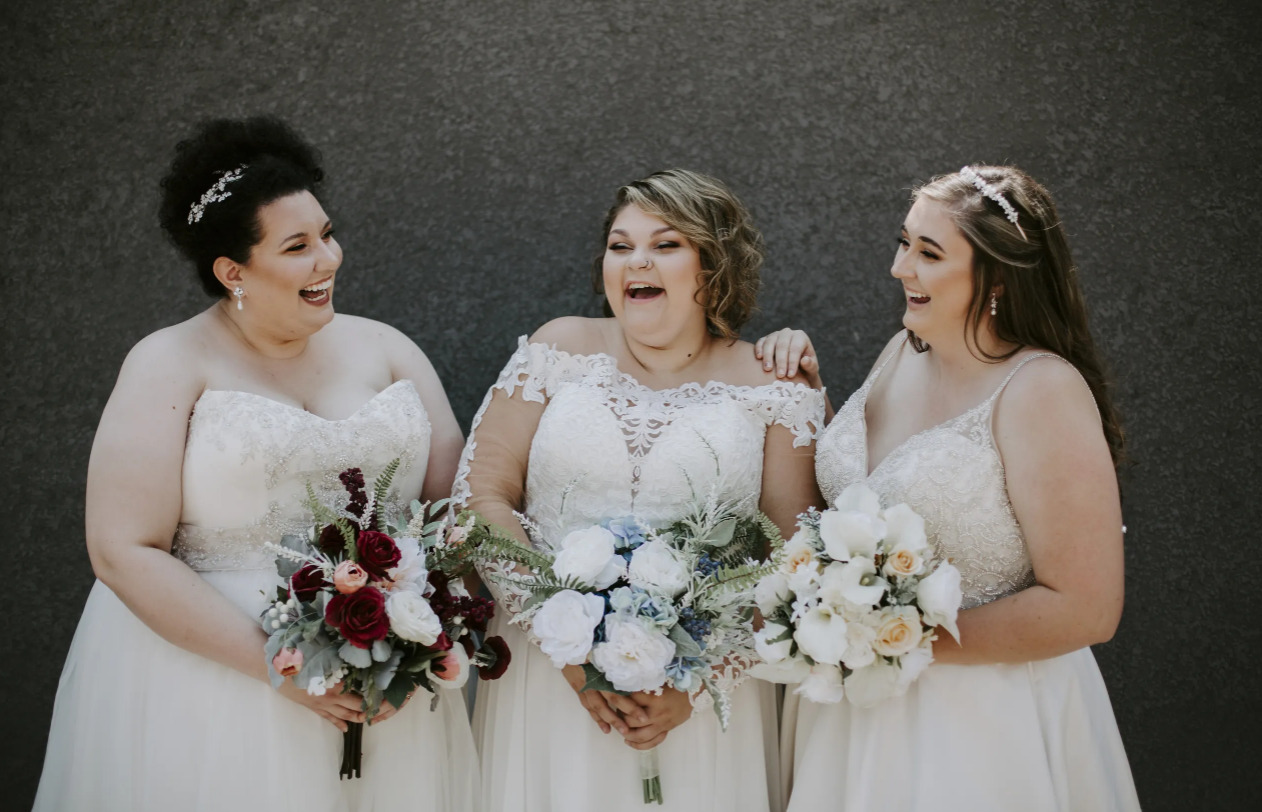 Three brides smile in their wedding dresses.