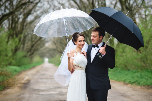 A bride and groom pose together with matching white and black umbrellas amid rain on their wedding day.