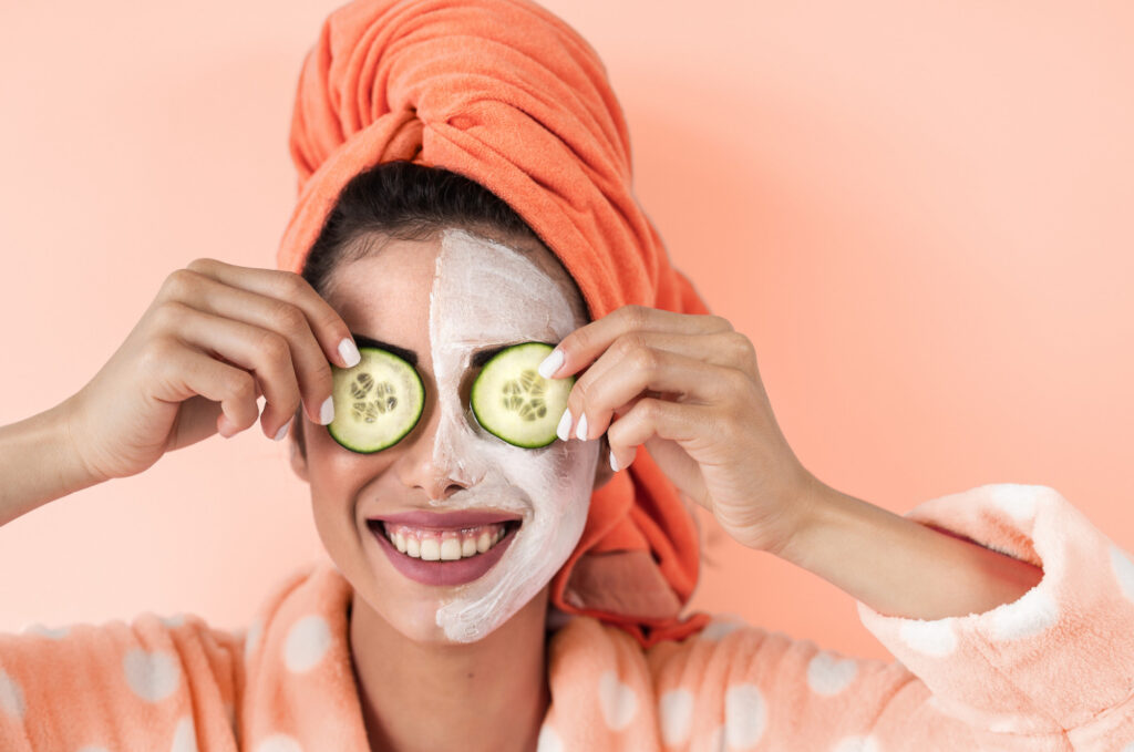Spa goer playfully smiles while covering her eyes with cucumber slices. Her hair is wrapped in a pink coordinating towel with her polka dotted robe.  
