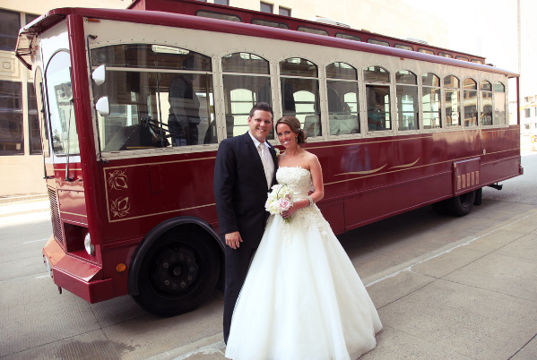 A bride and groom pose in front of a trolley.