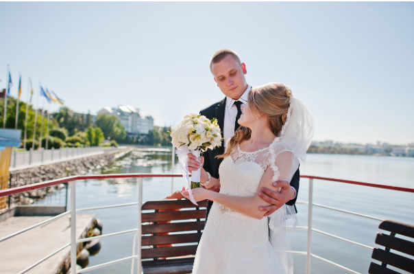 A bride and groom gaze into each other's eyes while posing on a big boat. 