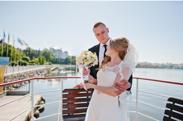 A bride and groom gaze into each other's eyes while posing on a big boat.