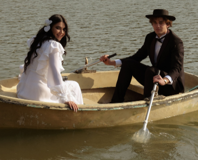 A bride smiles as she sits in the front of a row boat rowed by her groom.