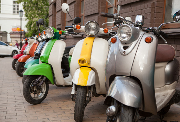 Colorful mopeds line up while parked on the side of the road.