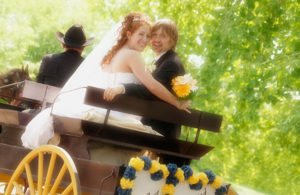 A bride and groom smile behind their backs while riding upon a horse drawn carriage. 