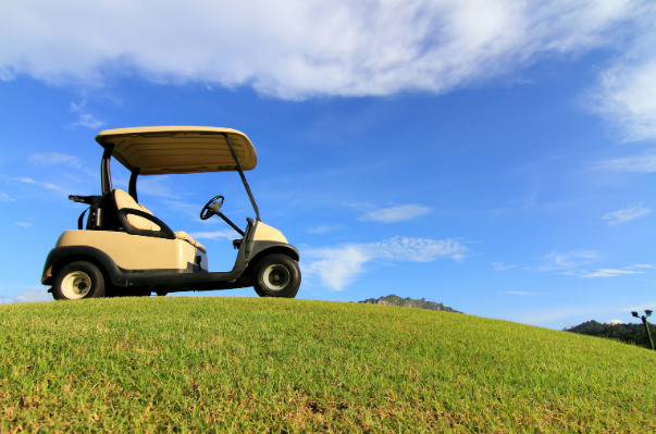 A golf cart sits upon a grass hill with a big blue sky.