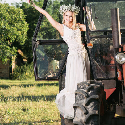 A bride poses with her flowers while standing upon a big tractor.