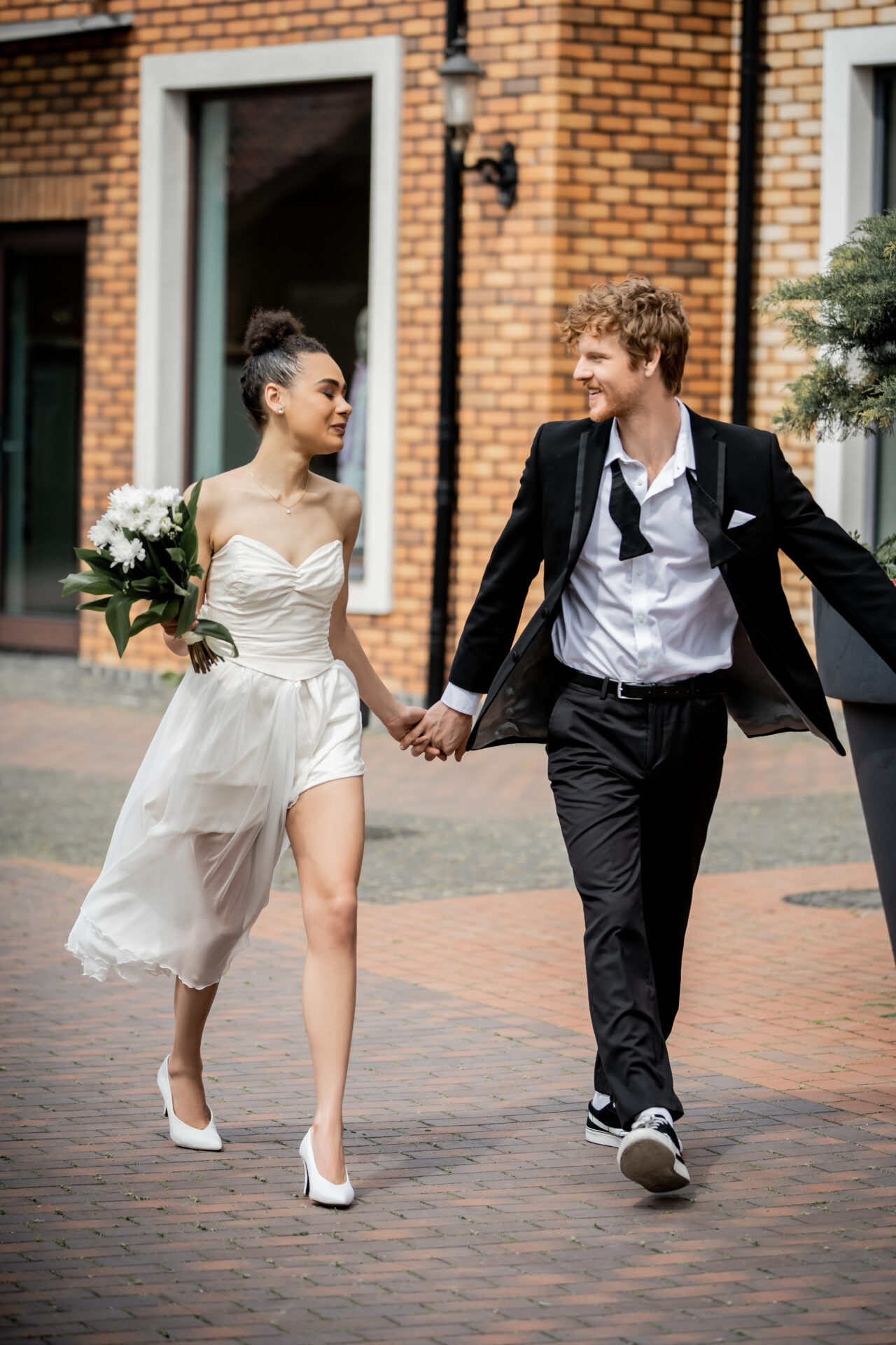 bride with flowers and groom in suit walking in city
